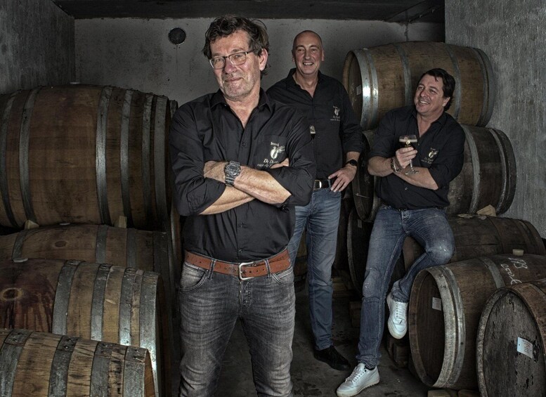 Three men standing in a cellar with wooden barrels. 5