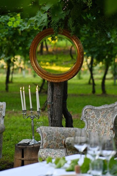 A rustic outdoor setting with a wooden table, a floral-patterned sofa, and a mirror on a tree trunk. 4