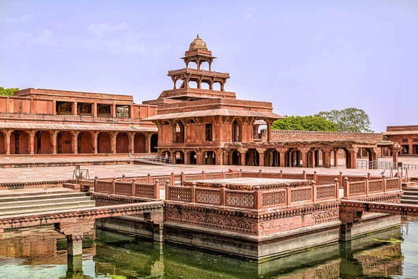 A historic building with a central tower, arched walkways, and a reflective water body. 4