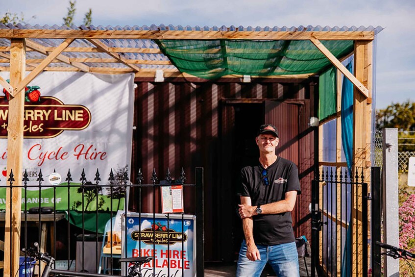 A man standing in front of a bike rental station with a banner advertising 'Merry Line' and 'Bike Hire Available'. 4