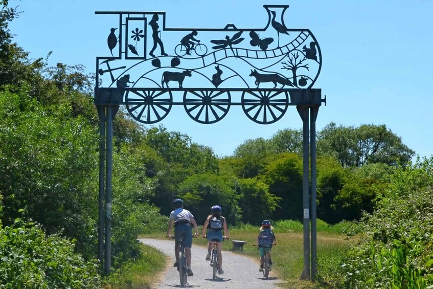 A metal archway with a vintage train motif, cyclists riding through a rural path. 3