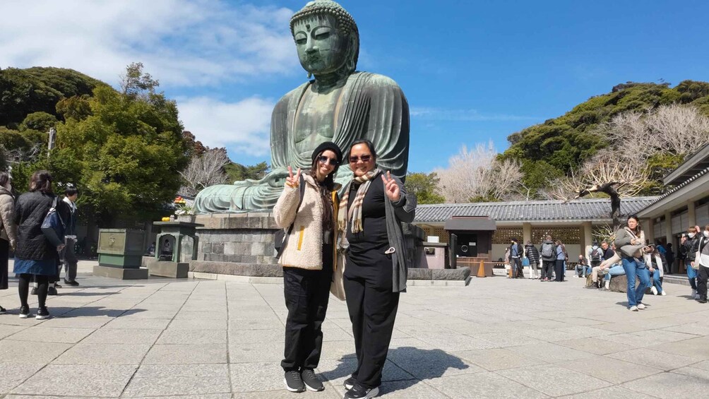Two people posing in front of a large Buddha statue with a traditional building in the background. 4
