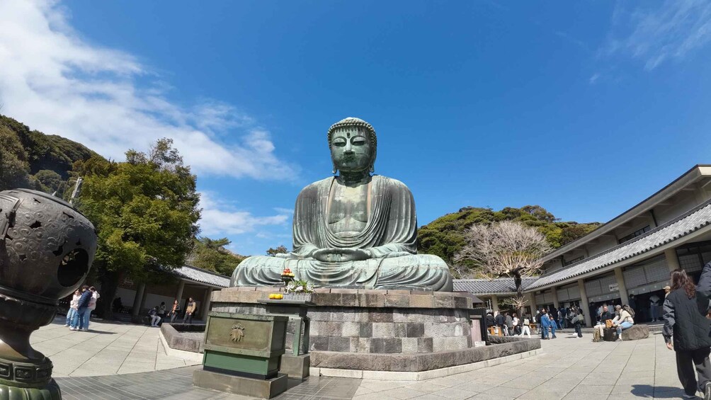 A large seated Buddha statue in a courtyard with visitors around. 3