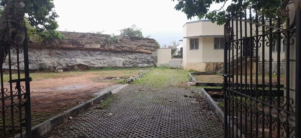 A paved pathway leading to a gated entrance, a stone wall, and a building with a flat roof. 2