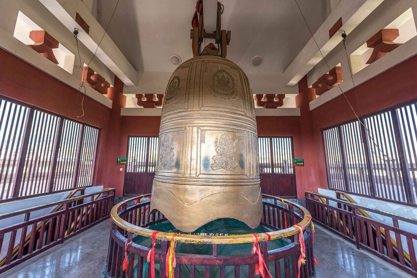 A large, ornate bell suspended in a room with red walls and barred windows. 4