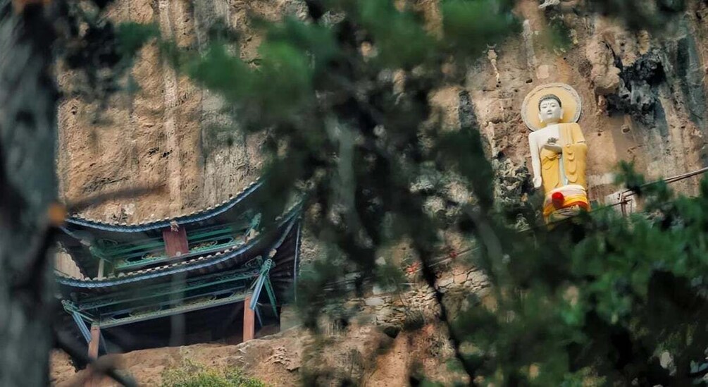 A large Buddha statue on a cliff, with a traditional building in the foreground. 2