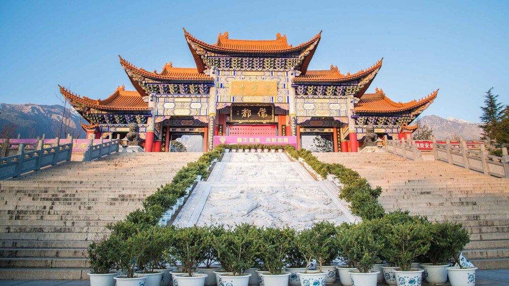 A traditional Chinese gate with ornate architecture, a stone staircase leading up to it, and potted plants in the foreground. 3