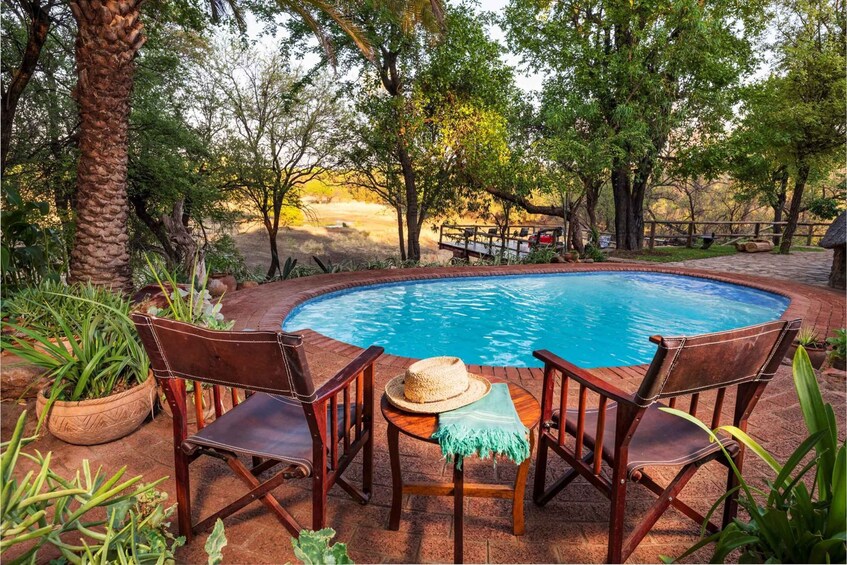 A swimming pool with two wooden chairs and a straw hat on one of them. 5