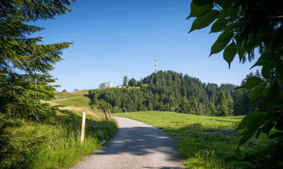 A gravel path leading to a hill with a building and a tall structure on top. 3