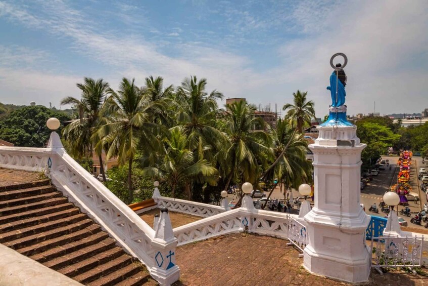 A white staircase with balusters, a statue with a blue figure, and palm trees in the background. 5