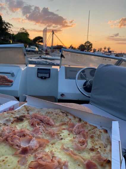 A boat's interior with a pizza box containing a pizza topped with ham. 2