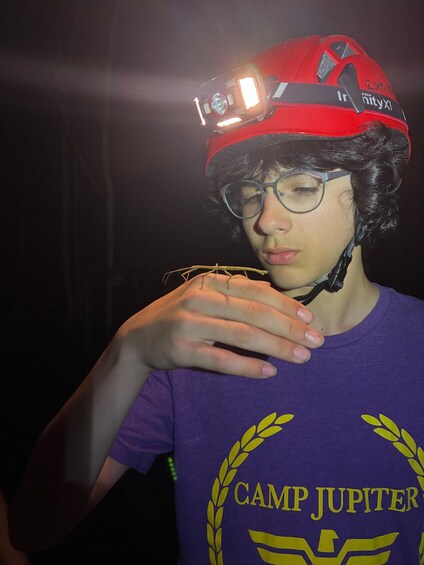 A person wearing a red helmet with a mounted light and a purple t-shirt with 'CAMP JUPITER' text. 5