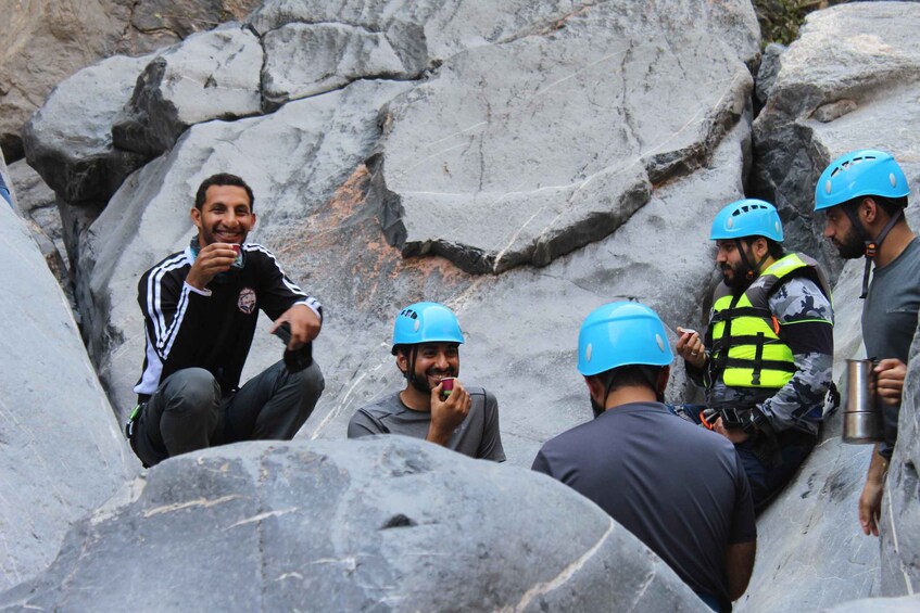 A group of people wearing helmets and safety gear, sitting and standing on rocky terrain. 3