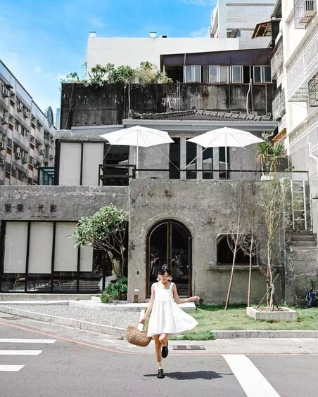 A person in a white dress walking on a street with umbrellas and a building in the background. 5