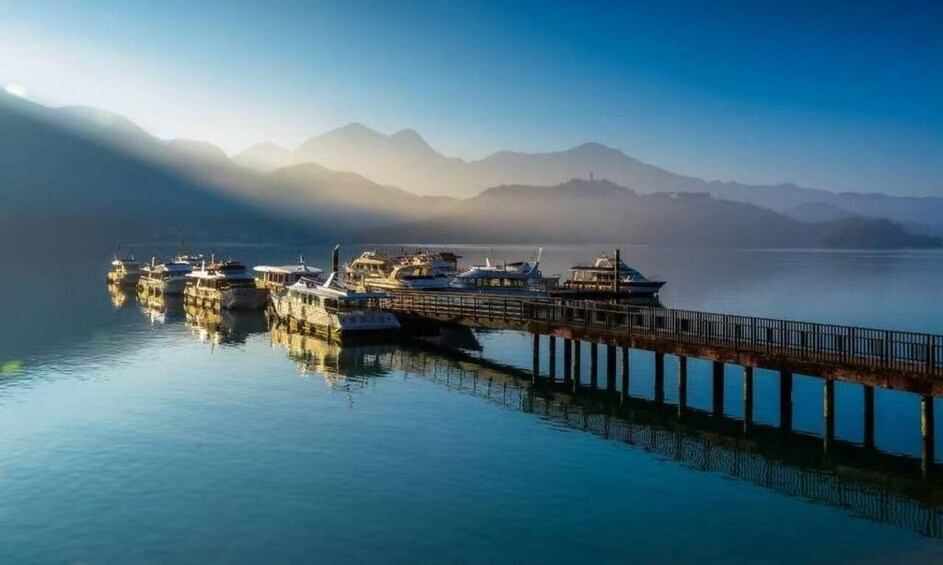 A calm lake with boats docked at a pier, surrounded by mountains. 3