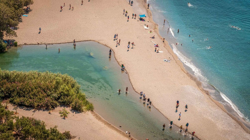 A beach with clear water, people walking, and a small pond. 2