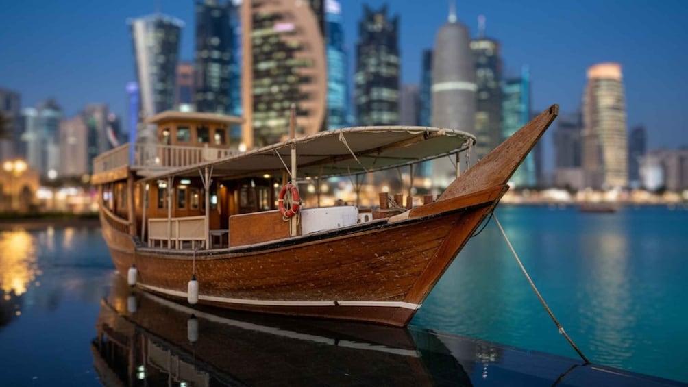 A traditional wooden boat with a canopy, docked near a modern city skyline with tall buildings. 1