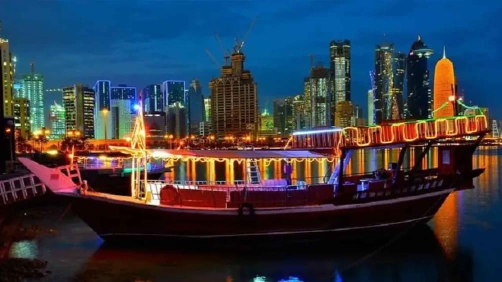 A boat with a lit-up structure in the foreground and a city skyline with illuminated buildings in the background. 5