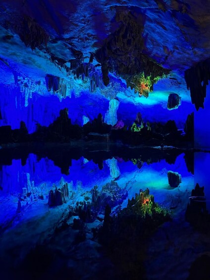 En hule med stalaktitter og stalagmitter belyst af blåt lys, der reflekteres i vandoverfladen. 5