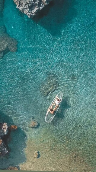 An aerial view of a clear blue sea with a person paddling a kayak. 1