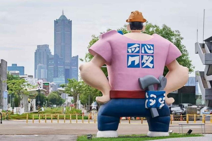 A large inflatable statue of a man with a pink shirt and blue pants, standing on grass with a cityscape in the background. 4