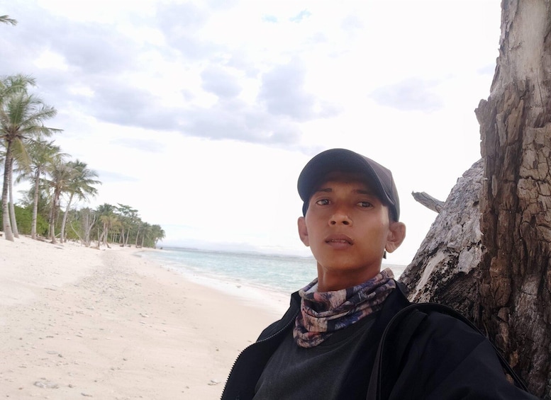 A person standing on a sandy beach with palm trees and a rocky cliff in the background. 2