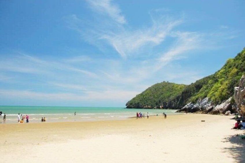 A beach with people, a clear sky, and a green hill in the background. 5