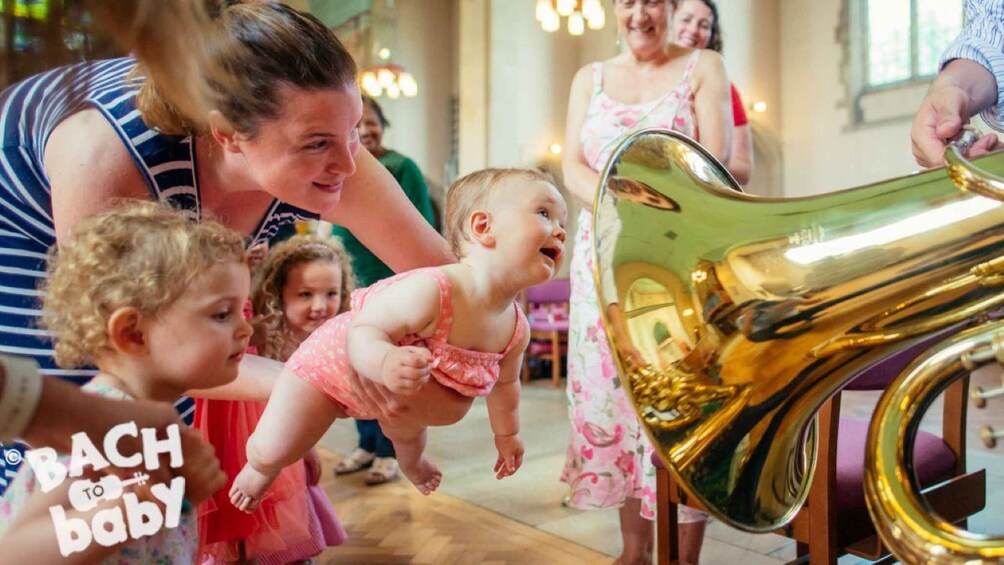 A brass musical instrument, likely a tuba, with a group of children and adults around it. 1
