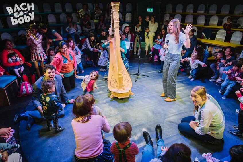 A group of people, including children, gathered around a large golden musical instrument in a performance setting. 4