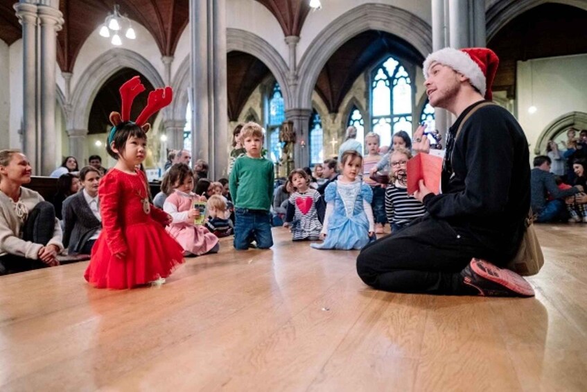 A person in a Santa hat sitting on the floor in a church with children around. 2