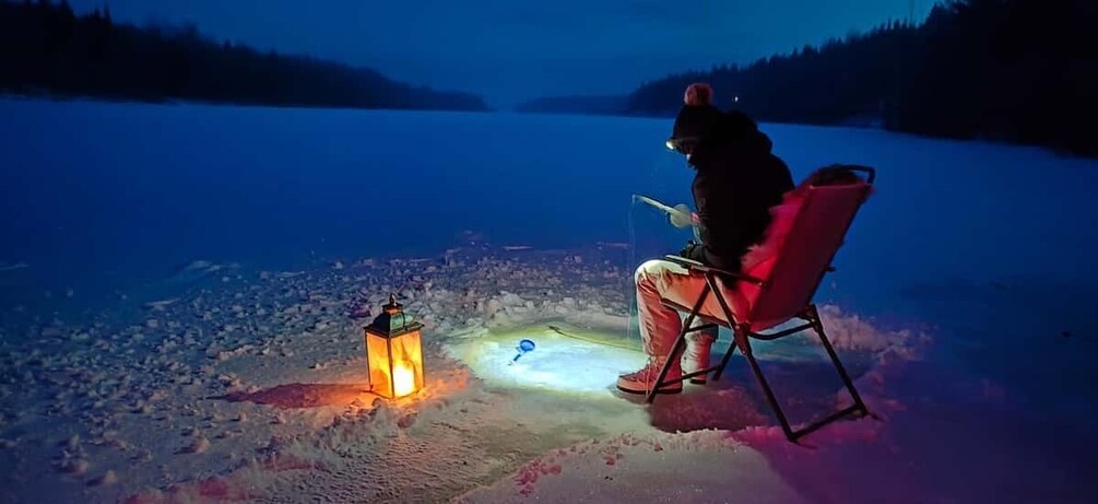 A person sitting on a red chair by a campfire in a snowy landscape. 1