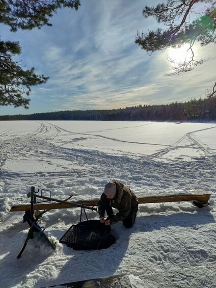 A person clearing snow from a sled on a frozen lake with trees in the background. 4