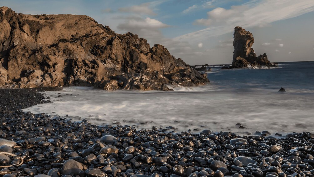 A rocky shoreline with large boulders and a prominent rock formation in the water. 2