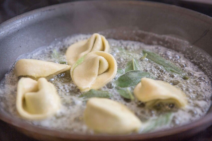 Ravioli being fried in a pan with some green herbs. 3