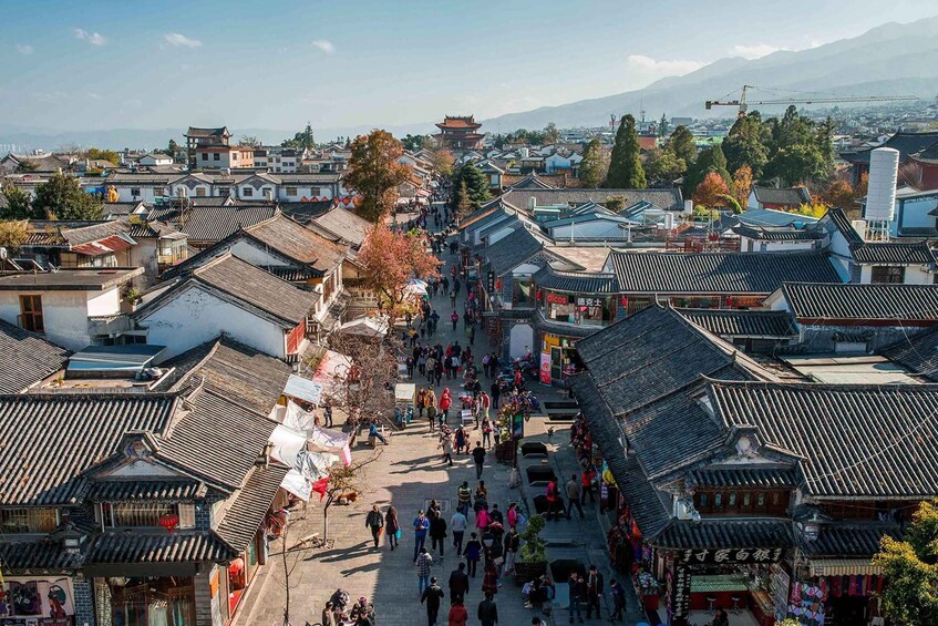 A traditional street lined with buildings, a crowd of people, and a mountain in the background. 2