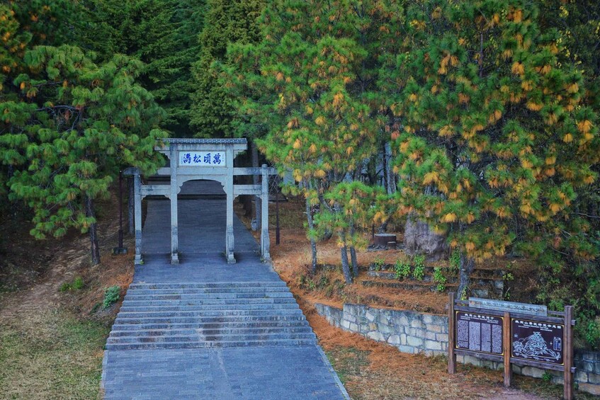 A stone staircase leading to a traditional gate with a sign in a forested area. 1
