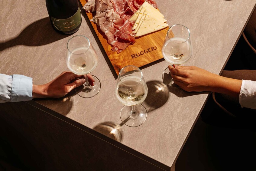 A table with a bottle of wine, cheese, cured meats, and glasses of white wine. 1