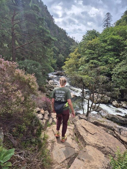 A person hiking on a rocky path with a river and forested hills in the background. 2