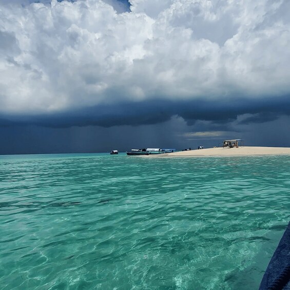 A beach with clear turquoise water, a sandy shore, and a few boats. 1