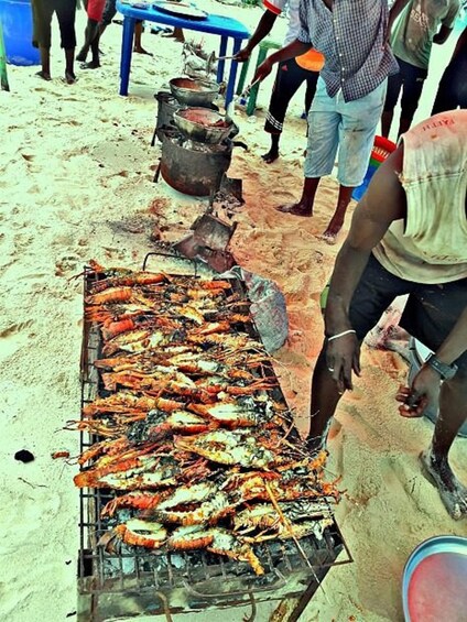 A grill with cooked seafood, a blue table, and people around. 4