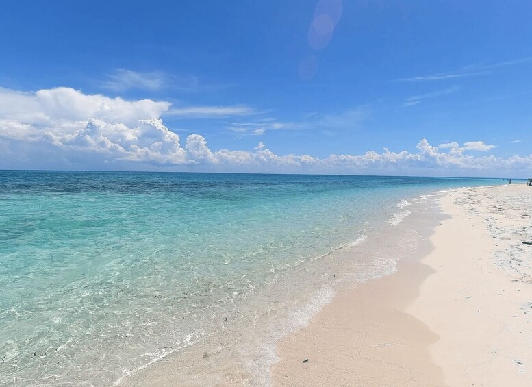 A beach with clear turquoise water, a sandy shore, and a partly cloudy sky. 5