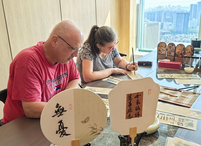 Two people practicing calligraphy with traditional brushes and paper. 1