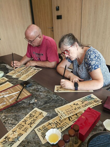 Two people practicing calligraphy on paper with brushes and ink. 4