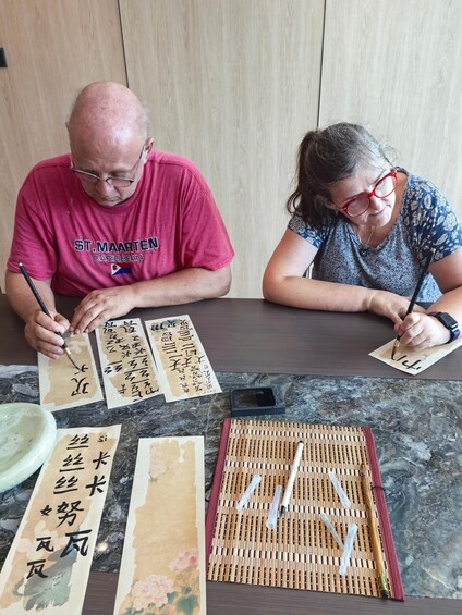 Two people writing Chinese characters on paper with brushes. 2