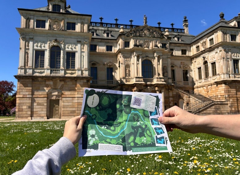 A person holding a map in front of a large, ornate building with a garden in the foreground. 3