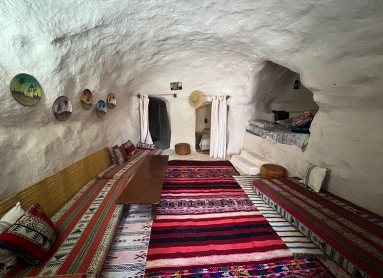 An ice hotel interior with a wooden bench, colorful rugs, and a small table. 4