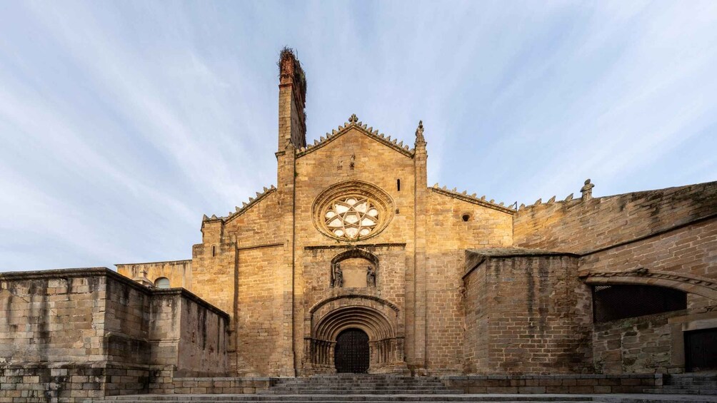 A historic stone church with a large circular stained glass window, a tall bell tower, and a series of arches. 2