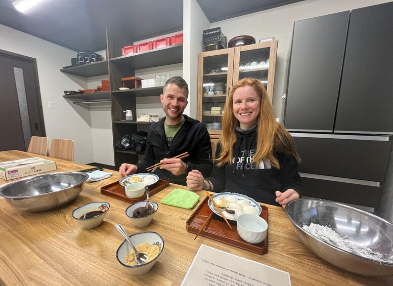 Two people sitting at a wooden table with bowls of food, chopsticks, and a menu. 5