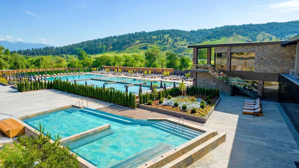 A pool area with multiple swimming pools, lounge chairs, and a modern building. 1