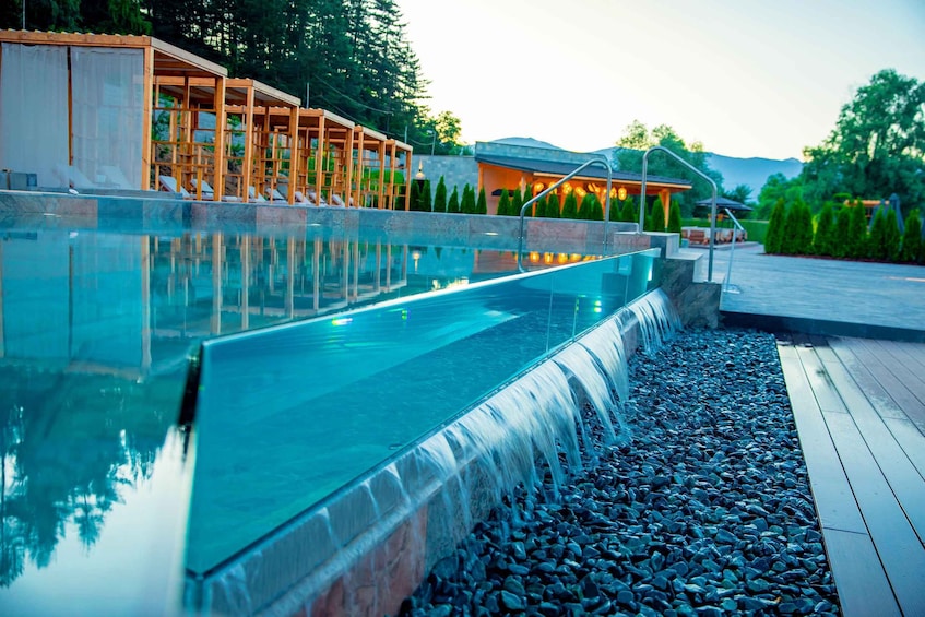 A swimming pool with a waterfall feature, surrounded by wooden structures and a pebble-lined deck. 5